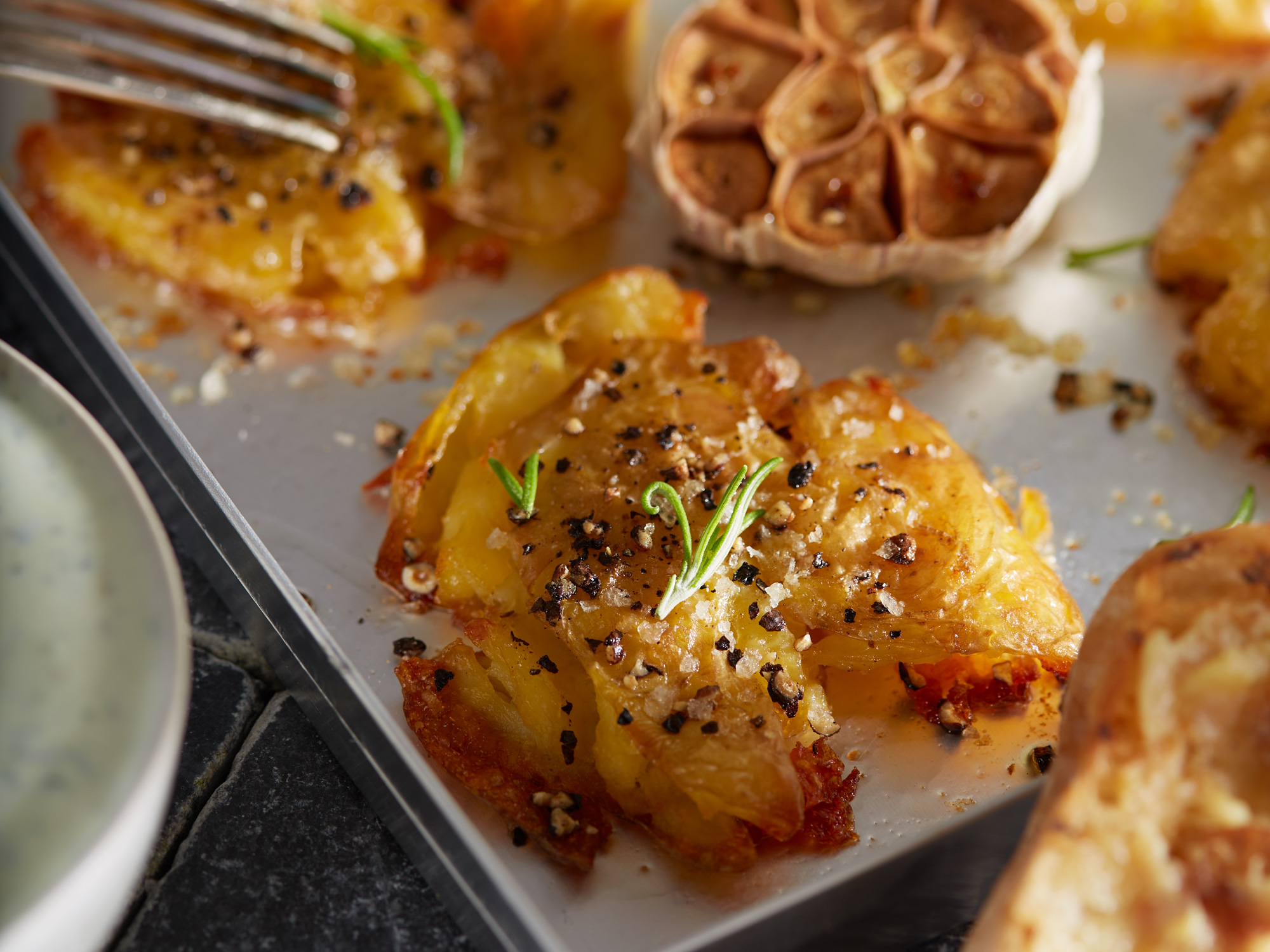 Nahaufnahme von knusprigen Smashed Potatoes mit Knoblauch und Rosmarin.