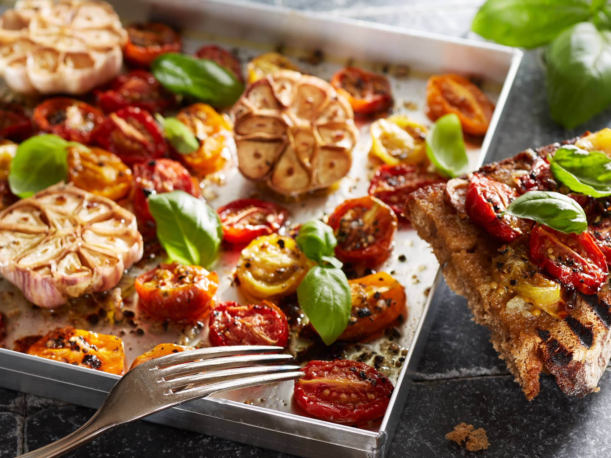 Cocktailtomaten aus dem Ofen mit Basilikum und Knoblauch auf gegrilltem Schwarzbrot.