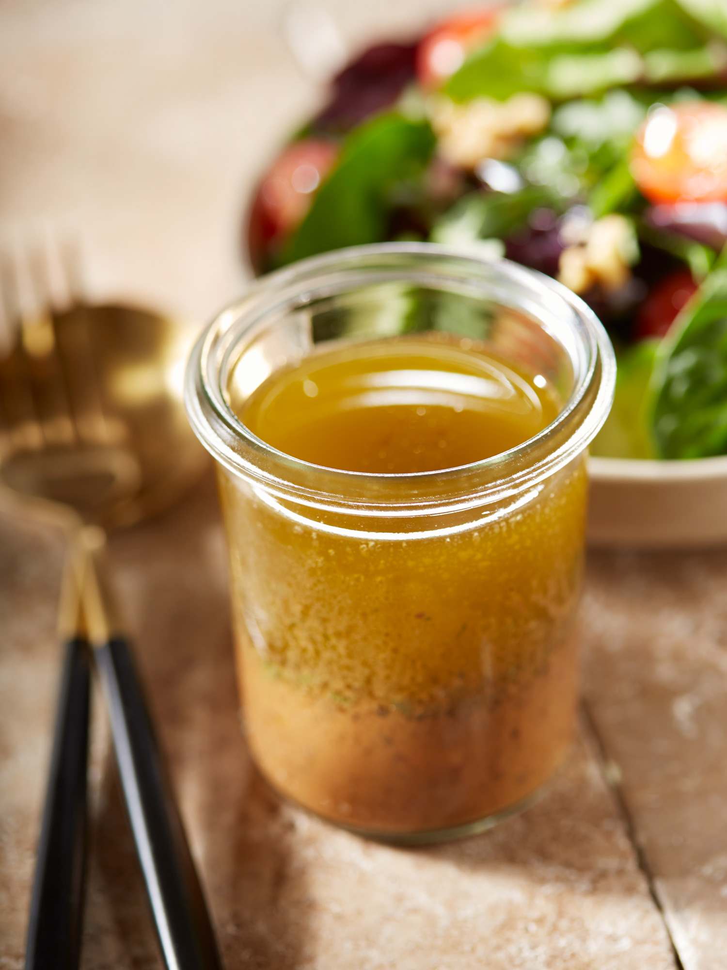 Salatdressing mit Honig und Senf, im Hintergrund unscharf eine Schüssel mit gemischtem Salat.