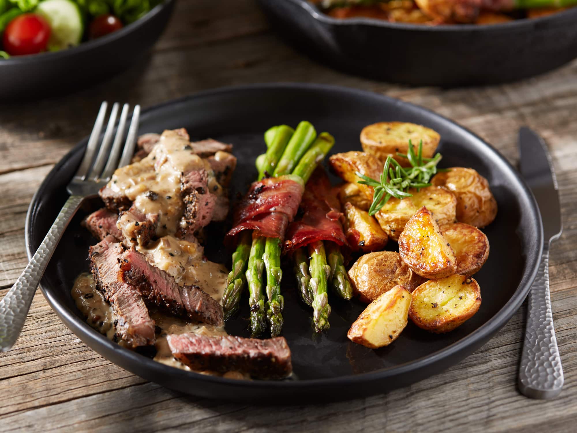Rindersteak mit Pfeffersauce, Rosmarinkartoffeln und grünem Spargel.