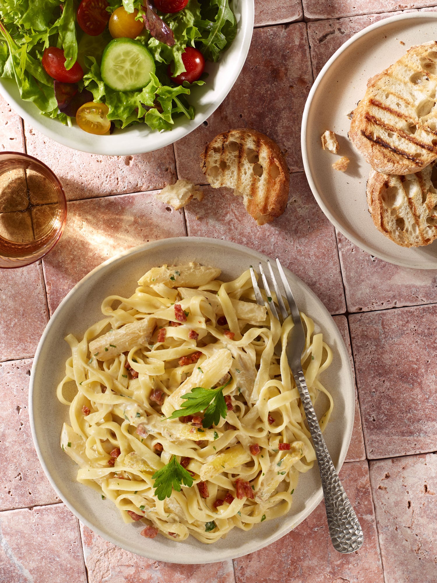 Pasta mit weißem Spargel und knusprigen Speckwürfeln in Sahnesauce, mit frischer Petersilie, dazu ein kleiner Beilagensalat und gegrillte Baguettescheiben.