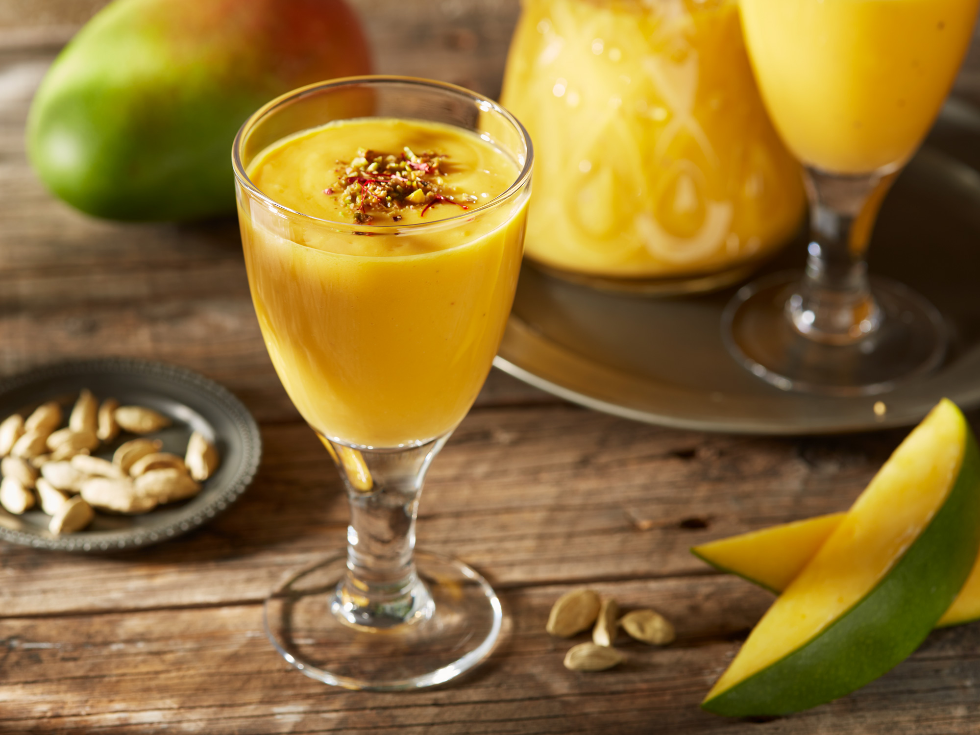 Mango Lassi mit frischer Mango und grünem Kardamom, garniert mit gehackten Pistazien und Safranfäden.